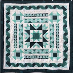May include: A quilt with a starburst pattern in shades of green and white. The quilt is made up of various geometric shapes and is surrounded by a border of green and white.