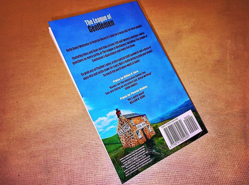 May include: The back cover of a book titled "The League of Gentlemen". The cover features a blue sky with white clouds and a small stone building with a sign that reads "Local Shop". The text on the cover describes the book as a series of questions and answers, including a quiz, and includes praise for the book from John Landis and Killian R. Gore.