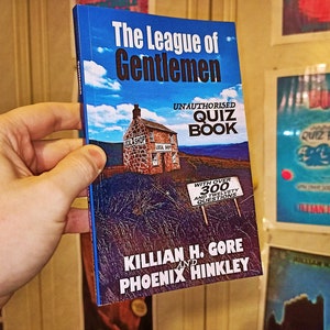 May include: A blue book titled "The League of Gentlemen Unauthorised Quiz Book" with a picture of a stone house and a sign that says "With over 300 and twelvey questions". The book is by Killian H. Gore and Phoenix Hinkley.