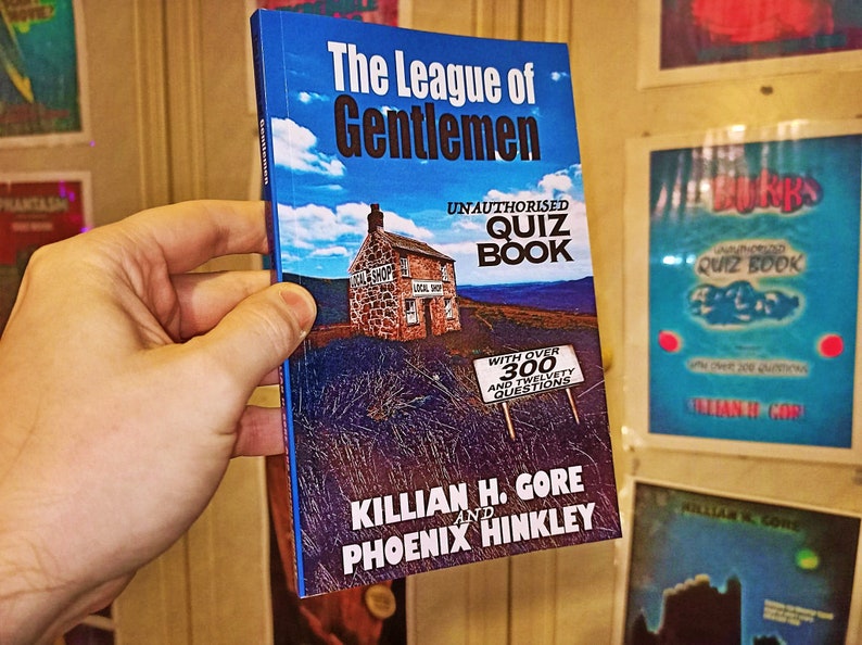 May include: A blue book titled "The League of Gentlemen Unauthorised Quiz Book" with a picture of a stone house and a sign that says "With over 300 and twelvey questions". The book is by Killian H. Gore and Phoenix Hinkley.