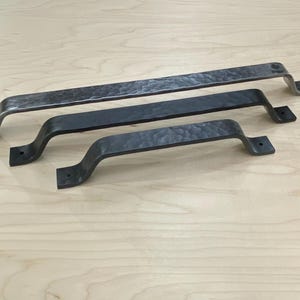 May include: Three black metal door handles of different sizes. The handles are made of a hammered metal and have a rustic look.