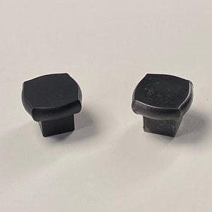 May include: Two black square cabinet knobs with rounded edges.