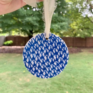 May include: A white ceramic ornament with a blue and white geometric pattern. The ornament is round and has a hole at the top for hanging.