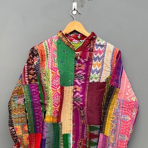 Może przedstawiać: Kolorowa pikowana kurtka w stylu patchwork z kołnierzem mandaryńskim i zapięciem na guziki. Kurtka jest wykonana z różnych tkanin w odcieniach różowego, fioletowego, zielonego, niebieskiego i czerwonego.