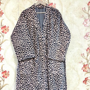 May include: A pink and black leopard print robe with a black and white striped lining. The robe has a tie belt and long sleeves.