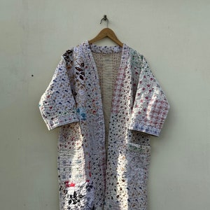 Könnte beinhalten: Eine weiße gesteppte Robe mit Blumenmuster. Die Robe ist aus Patchwork-Stoff gefertigt und hat eine lange, fließende Silhouette.
