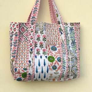 Op de afbeelding: Een patchwork tote bag met roze, blauwe en groene bloemenpatronen. De tas heeft lange hengsels en is gemaakt van gestikt stof.