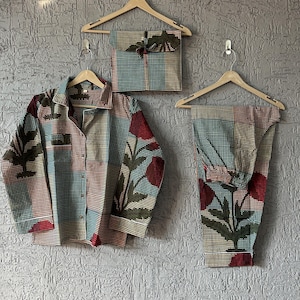 Peut inclure: Un ensemble de pyjama assorti avec un motif floral rouge, turquoise et vert. L'ensemble comprend une chemise boutonnée, un pantalon et un article emballé assorti, le tout suspendu à des cintres en bois sur un mur gris texturé.