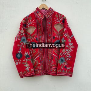 Könnte beinhalten: Rote Jacke mit aufwendiger Blumenstickerei in Blau-, Beige- und Grüntönen. Die Jacke hat einen hohen Kragen und hängt an einem Holzbügel. Der Text "TheIndianvogue" ist auf der Jacke zu sehen.