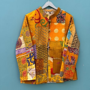 May include: A yellow quilted jacket with a patchwork design featuring various colors and patterns. The jacket has a mandarin collar and a button closure.