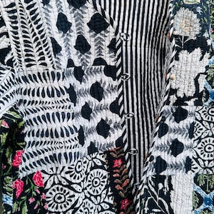 Pode incluir: Uma jaqueta acolchoada preta e branca com estampa floral. A jaqueta tem fecho de botão e decote em V.