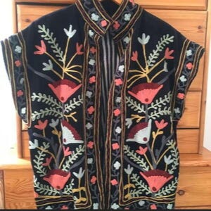 Puede incluir: Chaqueta azul marino oscuro de manga corta con intrincados bordados florales. El bordado presenta flores y hojas rojas, rosas, amarillas y blancas. La chaqueta tiene cuello y un diseño de rayas verticales en el centro.