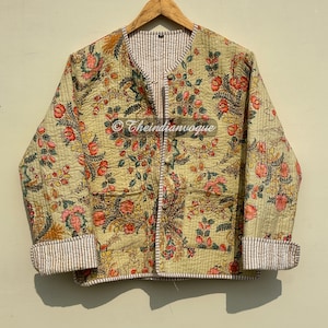 May include: A beige quilted jacket with a floral print and a brown and white striped lining. The jacket has a button closure and a V-neck.