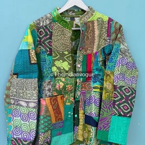 Pode incluir: Uma jaqueta patchwork colorida em tons de verde, roxo e laranja pendurada em um cabide branco. A jaqueta apresenta uma variedade de tecidos estampados, incluindo desenhos florais e geométricos. O texto "Theindianvogue" é visível. A jaqueta é acolchoada e tem fechamento por botões.