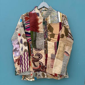 May include: A patchwork quilted jacket with a mandarin collar and long sleeves. The jacket is made of various fabrics in shades of brown, red, purple, and green. The fabric is patterned with floral designs, paisley, and geometric shapes.