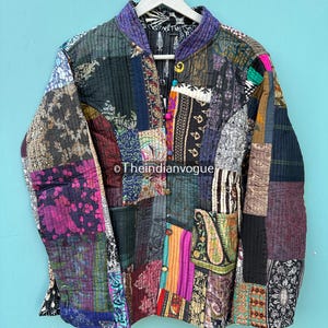 Pode incluir: Casaco patchwork multicolorido com uma variedade de padrões de tecido. O casaco tem gola mandarim, fecho de botões e bolsos. O texto "Theindianvogue" é visível no casaco. O casaco está pendurado num cabide branco.