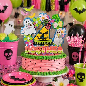 May include: A pink frosted cake with a watermelon design, topped with a colorful Halloween-themed decoration and the name "DORTHEA". The cake is surrounded by pink and green party supplies, including plates, cups, and balloons.
