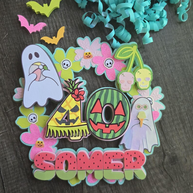May include: A colorful Halloween-themed papercraft design featuring ghosts, bats, flowers, and fruit. The word "SOMER" is displayed in watermelon-style letters. The design includes a pineapple, watermelon, and cherries with skull faces.
