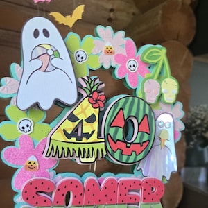 May include: A colorful Halloween-themed decoration with the word "SOMER" in watermelon-style letters. The design includes ghosts, bats, flowers, and a pineapple with the number "40".