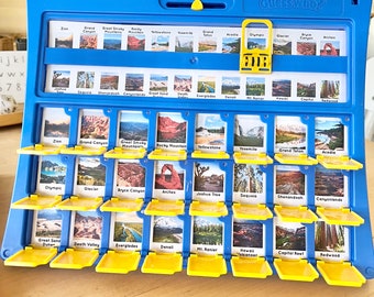 Könnte beinhalten: Blaues "Wer bin ich?" Brettspiel mit Bildern von Nationalparks und Sehenswürdigkeiten. Das Spiel hat einen blauen Rahmen, gelbe Schiebetüren und einen gelben Wahlschalter. Das Spiel enthält Bilder von Zion, Grand Canyon und Yosemite.