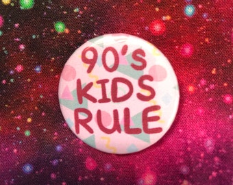 May include: A pink button with a 90's kids rule design. The button has a white background with a geometric pattern in pink, green, and yellow.