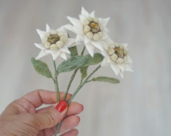 May include: A bouquet of three white felt edelweiss flowers with green felt stems and leaves.