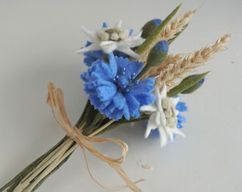 May include: A bouquet of felt flowers, including blue cornflowers and white edelweiss, tied with a brown raffia ribbon. The bouquet also includes wheat stalks and green leaves.