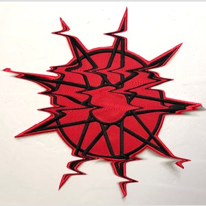 May include: Red and black embroidered patch with a starburst design. The starburst has a red center and black lines radiating outward.