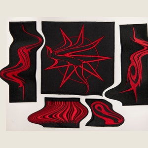 Puede incluir: Cinco parches de tela negra con diseños bordados en rojo. Los diseños incluyen una estrella de explosión, un remolino y un patrón similar a un código de barras.