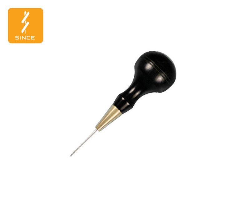 May include: A black and gold leather crafting tool with a wooden handle. The tool has a sharp, pointed tip.