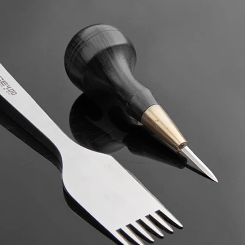 May include: A close-up of two leather working tools. A black handled awl with a brass ferrule and a silver stitching tool with six prongs.