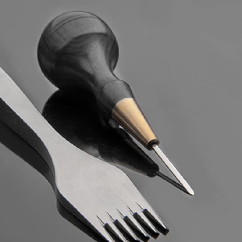 May include: A set of two leatherworking tools. One tool has a black wooden handle and a metal tip. The other tool has a metal handle and five prongs.
