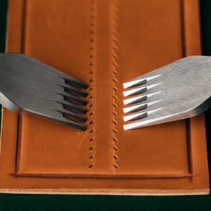 May include: Two silver leather stitching tools with multiple prongs are placed on a brown leather surface. The tools are used to create evenly spaced holes for stitching leather.
