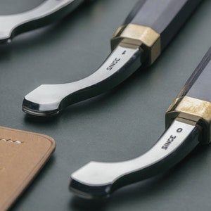 Könnte beinhalten: Zwei Werkzeuge mit schwarzen Griffen, silbernen Klingen und goldenen Akzenten. Die Werkzeuge sind mit den Worten "Since 0" und "Since 1" graviert.