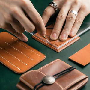 May include: A person uses a ruler to mark a piece of brown leather. The leather is being prepared for a craft project, such as a wallet or a phone case.
