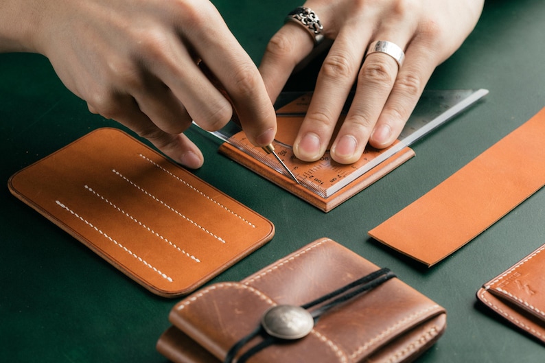 May include: A person uses a ruler to mark a piece of brown leather. The leather is being prepared for a craft project, such as a wallet or a phone case.