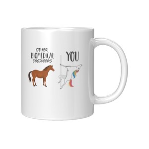 Può includere: Tazza da caffè in ceramica bianca con un'illustrazione in bianco e nero di un cavallo e un unicorno. Il testo "Other Biomedical Engineers" è sopra il cavallo e il testo "You" è sopra l'unicorno.