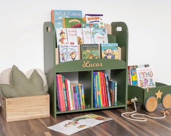 May include: A green wooden bookshelf with two shelves, labeled "Lucas", filled with children's books. A green toy wagon with a rope handle is on the floor next to the bookshelf.