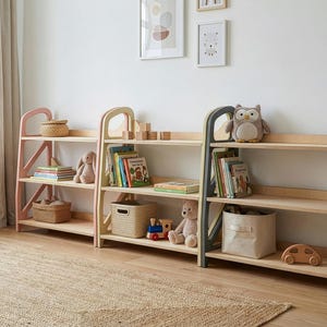 Three Montessori toy storage shelves in Dusty Blush, Vanilla Cream and Slate Gray used as kids bookshelf, nursery furniture and playroom decor along a bright kids room wall.