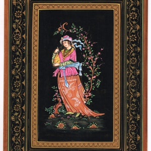 May include: A framed miniature painting depicting a woman in a pink and orange dress standing in a garden. The painting is set against a black background and has a gold and black frame.