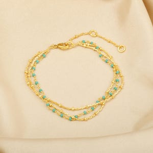 Puede incluir: Pulsera de cadena dorada con tres hileras de cuentas turquesas.