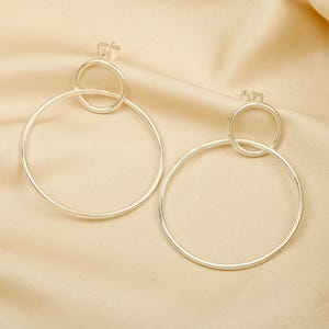 Puede incluir: Un par de pendientes de aro de plata con un círculo más pequeño dentro del círculo más grande.