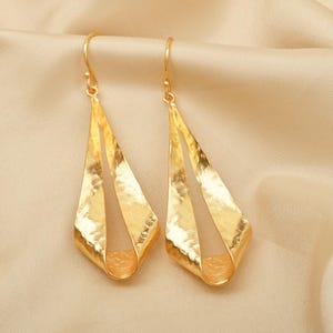 Peut inclure: Une paire de boucles d'oreilles pendantes dorées avec une finition martelée. Les boucles d'oreilles sont en forme de goutte d'eau avec un design incurvé et ouvert.