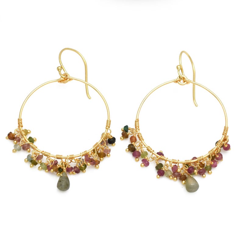 Puede incluir: Un par de pendientes de aro dorados. Cada pendiente presenta un grupo de peque&ntilde;as cuentas de colores en tonos rosa, verde y marr&oacute;n, con una piedra en forma de l&aacute;grima colgando de la parte inferior. Dise&ntilde;o sencillo y elegante.