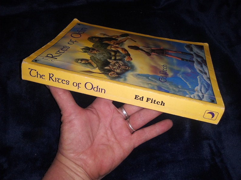 Może przedstawiać: Ż&oacute;łta książka w miękkiej oprawie zatytułowana "The Rites of Odin" autorstwa Ed Fitch. Okładka przedstawia kolorową ilustrację grupy ludzi w fantastycznym otoczeniu.