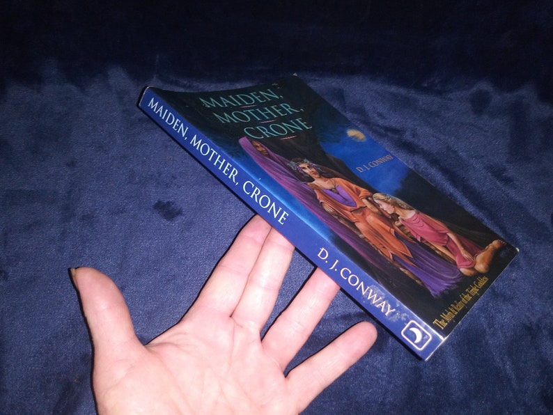 May include: A book titled "Maiden, Mother, Crone: The Mysteries of the Triple Goddess" by D.J. Conway. The cover features a painting of three women in flowing robes, set against a dark blue night sky with a crescent moon.