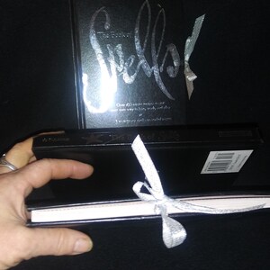 May include: Two black hardcover books with silver lettering. The larger book has the title "Sketch" and the smaller book is tied with a silver ribbon.