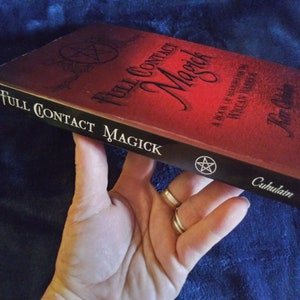 May include: A red book titled "Full Contact Magick" with a black pentagram on the cover. The book is a guide to Wiccan traditions.