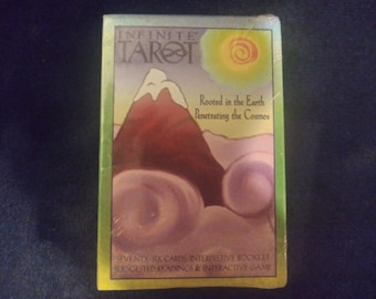 May include: A rectangular deck of Infinite Tarot cards in a box featuring a mountain with a snow-capped peak, a yellow sun, and swirling clouds. The text reads: Infinite Tarot, Rooted in the Earth, Penetrating the Cosmos, Seventy-Six Cards, Interpretive Booklet, Suggested Readings & Interactive Game.