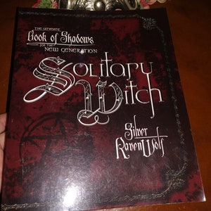 May include: The Ultimate Book of Shadows for the New Generation: Solitary Witch by Silver RavenWolf. A dark red book cover with silver lettering and a pentagram.